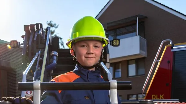 Kind mit neongelbem Feuerwehrhelm lächelt in die Kamera